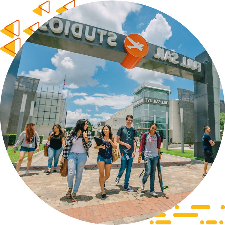 Four students casually chatting and walking under the Full Sail Studios archway, a blue sky with clouds in the background.